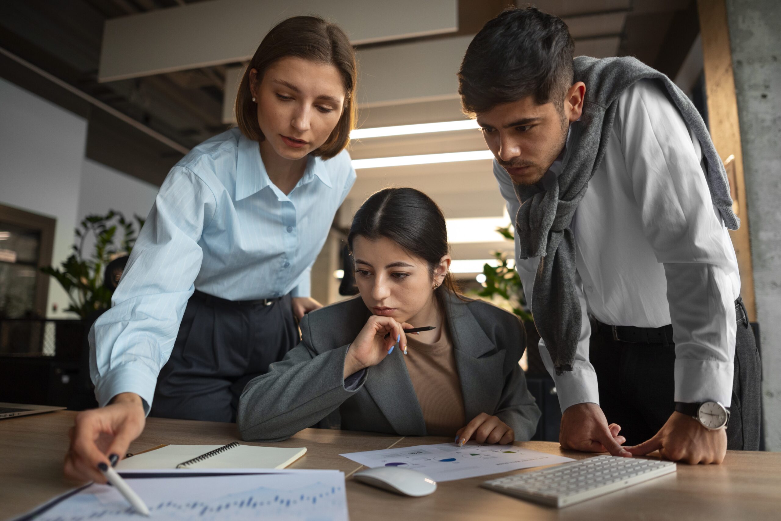 Professional financial partner reviewing client reports in a modern office while team members collaborate in the background.